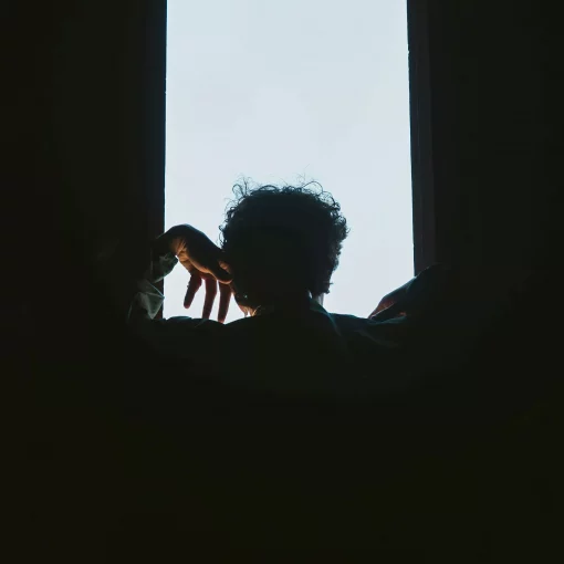 A person silhouetted against a bright window, creating a dramatic contrast between light and shadow.